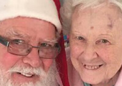 Smiling elderly woman with Santa Claus in festive attire.