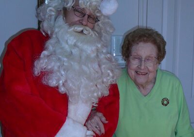 Santa Claus with an elderly woman smiling warmly indoors.