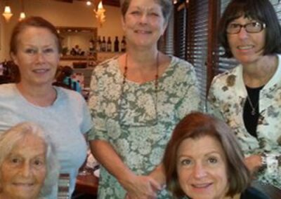 Five women smiling indoors at a social gathering.