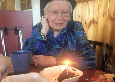 An elderly woman smiling at a birthday cake with a lit candle.