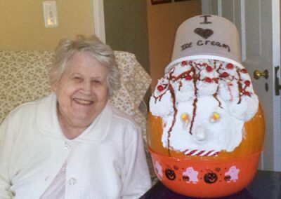 Elderly woman smiling beside a colorful autumn-themed cake.